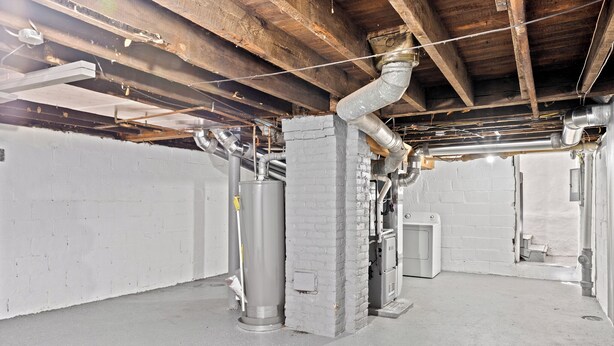 A basement with exposed ductwork, a large cylindrical tank, and a white brick wall. - Comfortable 2- Bedroom House In Cleveland 1330 (Cleveland)