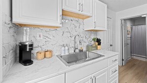 A modern kitchen with white cabinets, a marble backsplash, a built-in coffee maker, and a stainless steel sink. - Comfortable 2- Bedroom House In Cleveland 1330 (Cleveland)