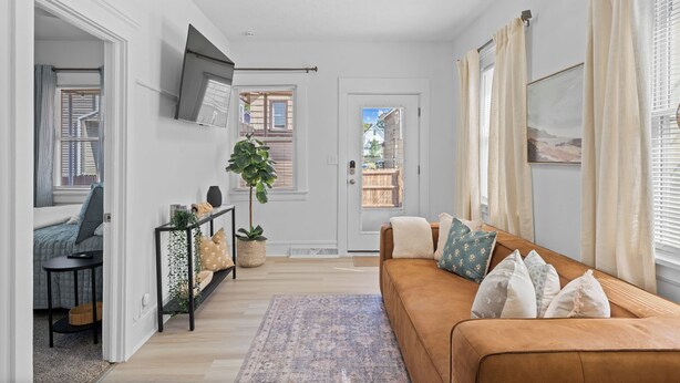 Uma sala de estar com um sofá marrom, uma TV fixada na parede e uma porta que dá para o exterior.