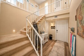 A multi-level interior with carpeted stairs, a white door, a small trash bin, and a wall-mounted map. - Melbourne Beach Oceanfront Apartment Unit #2 - Ocean Views (Melbourne Beach)
