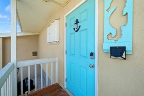 A turquoise door with an anchor symbol, a white railing, and a wall-mounted mailbox. - Melbourne Beach Oceanfront Apartment Unit #2 - Ocean Views (Melbourne Beach)
