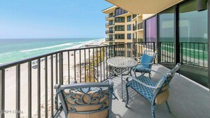 Un balcone con vista sulla spiaggia e sull'oceano, arredato con un tavolo e sedie, e un'ampia finestra.