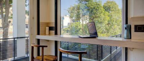 Una habitación moderna con un ventanal grande, una computadora portátil sobre un escritorio y dos sillas de madera.
