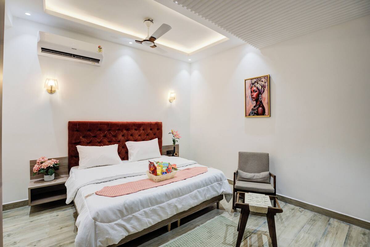 Une chambre moderne avec une tête de lit capitonnée, un lit agrémenté d’un panier décoratif rose, une table de chevet avec une lampe et une chaise.