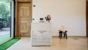 Ein Zimmer mit Holztür, einem weißen Schrank, einem kleinen Tisch mit einer Statue und Blick durch ein großes Fenster.