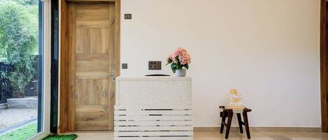 Una habitación con una puerta de madera, un mueble blanco de almacenamiento, una pequeña mesa con una estatua y vistas a través de un ventanal grande.