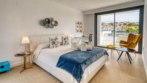 Camera da letto moderna con un letto grande, una scrivania e una sedia. Si vede una finestra con vista sulle case.