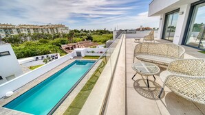 Area piscina sul tetto con vista panoramica sulla città, tra cui un edificio moderno e un complesso residenziale.