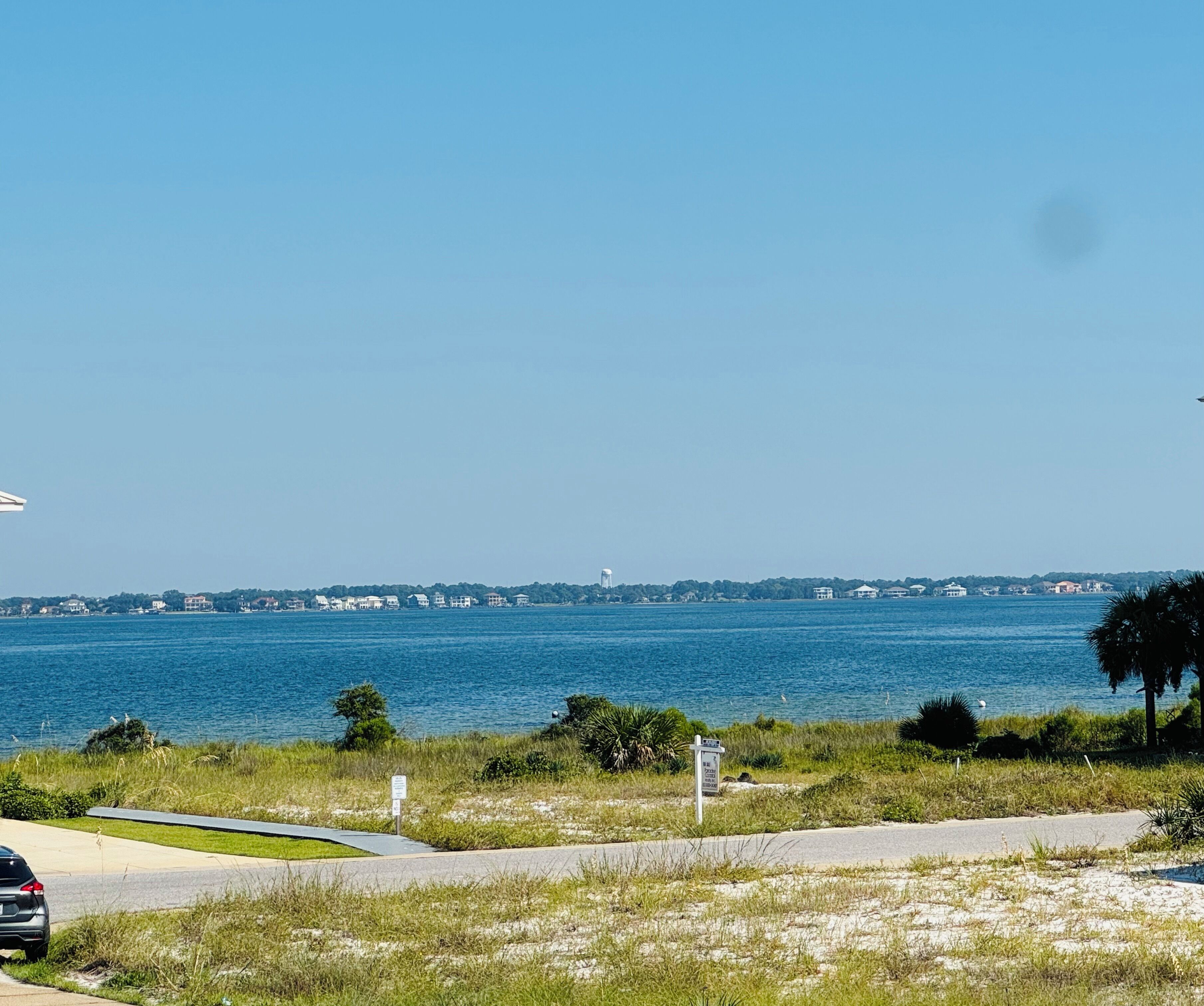 A coastal view with a road leading to a beach, a water tower, and a distant shoreline with buildings.
