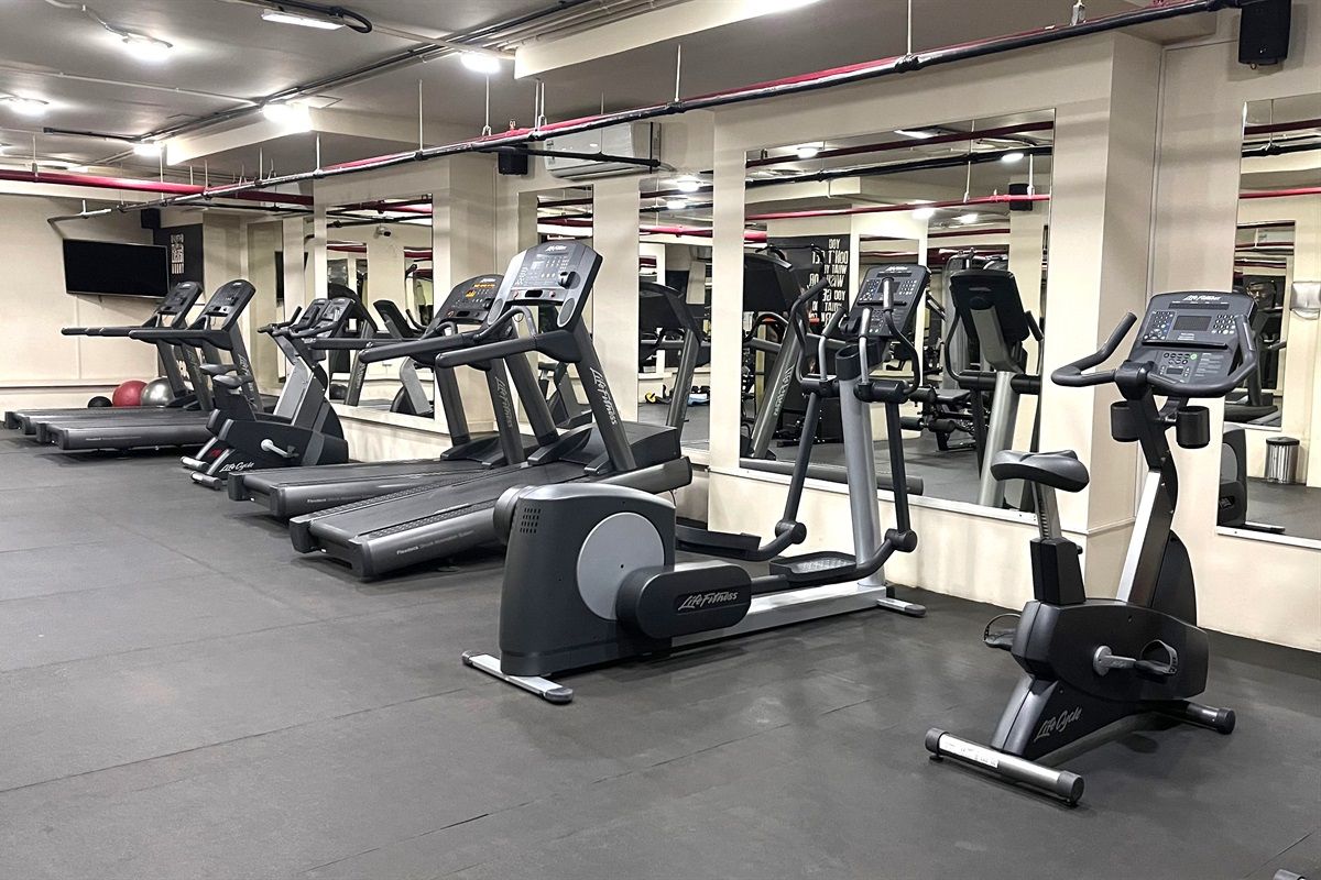 Une salle de sport équipée de nombreux appareils de cardio, notamment des tapis de course et des vélos elliptiques, disposés en rangées.