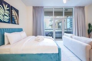 A hotel room with a bed, a sofa, a balcony with a table, and a city view. - Modern Comfort Studio Near Downtown Dubai (Dubai)