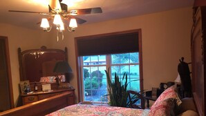 A bedroom with a large bed, a dresser, a mirror, a ceiling fan, and a window with a view of the outdoors.
