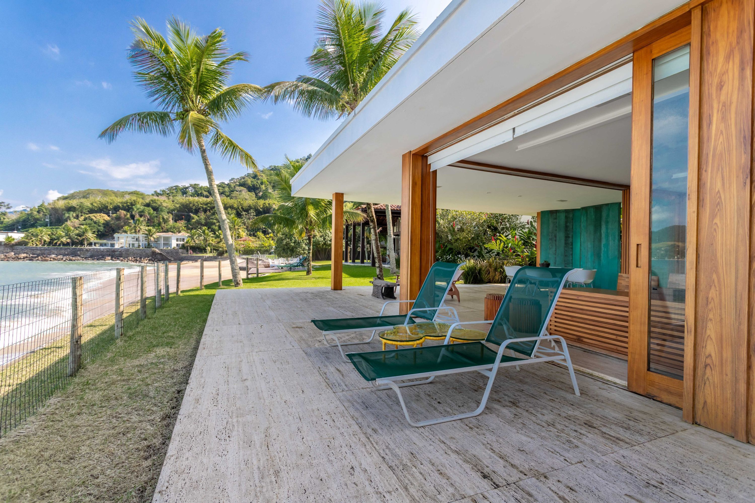 Un espacio lounge moderno al aire libre con sillas de vidrio y una terraza de madera con vista a una playa.