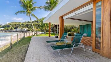 Un espacio lounge moderno al aire libre con sillas de vidrio y una terraza de madera con vista a una playa.