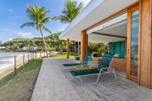 Un espacio lounge moderno al aire libre con sillas de vidrio y una terraza de madera con vista a una playa.