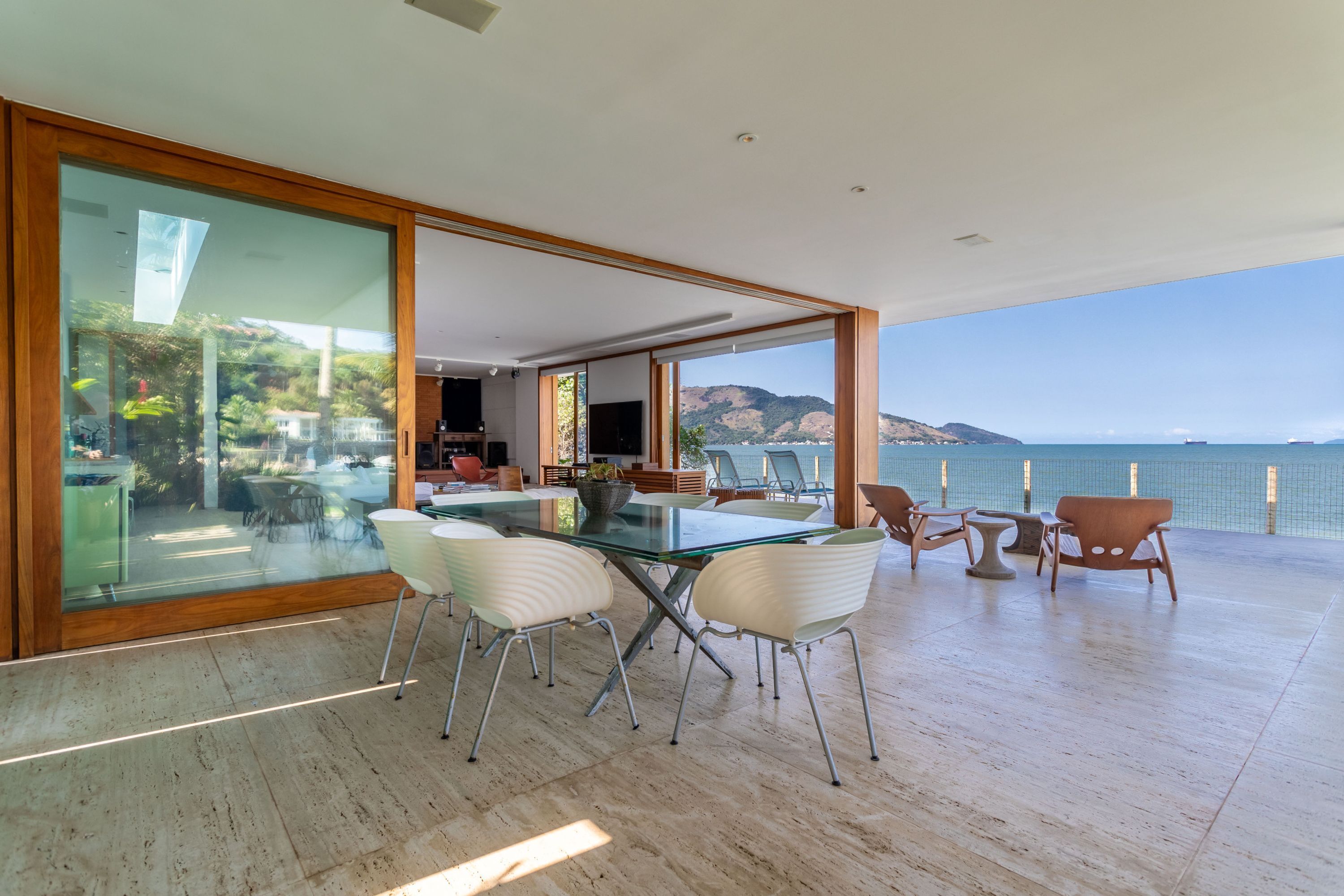 Un comedor amplio con una mesa y sillas de vidrio, con vistas panorámicas al mar y las colinas.