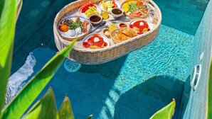 A poolside area with a wicker table holding a variety of food items, two wicker lounge chairs, and a potted plant.