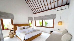 A bedroom with a large bed, a sofa, and a window with a view of greenery.