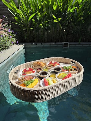 Un plateau de petit-déjeuner flottant, avec divers aliments et boissons, placé près d’une piscine.