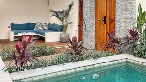 Un espace aménagé au bord de la piscine, avec une terrasse en bois, un coin salon doté d’un canapé et un mur en pierre.