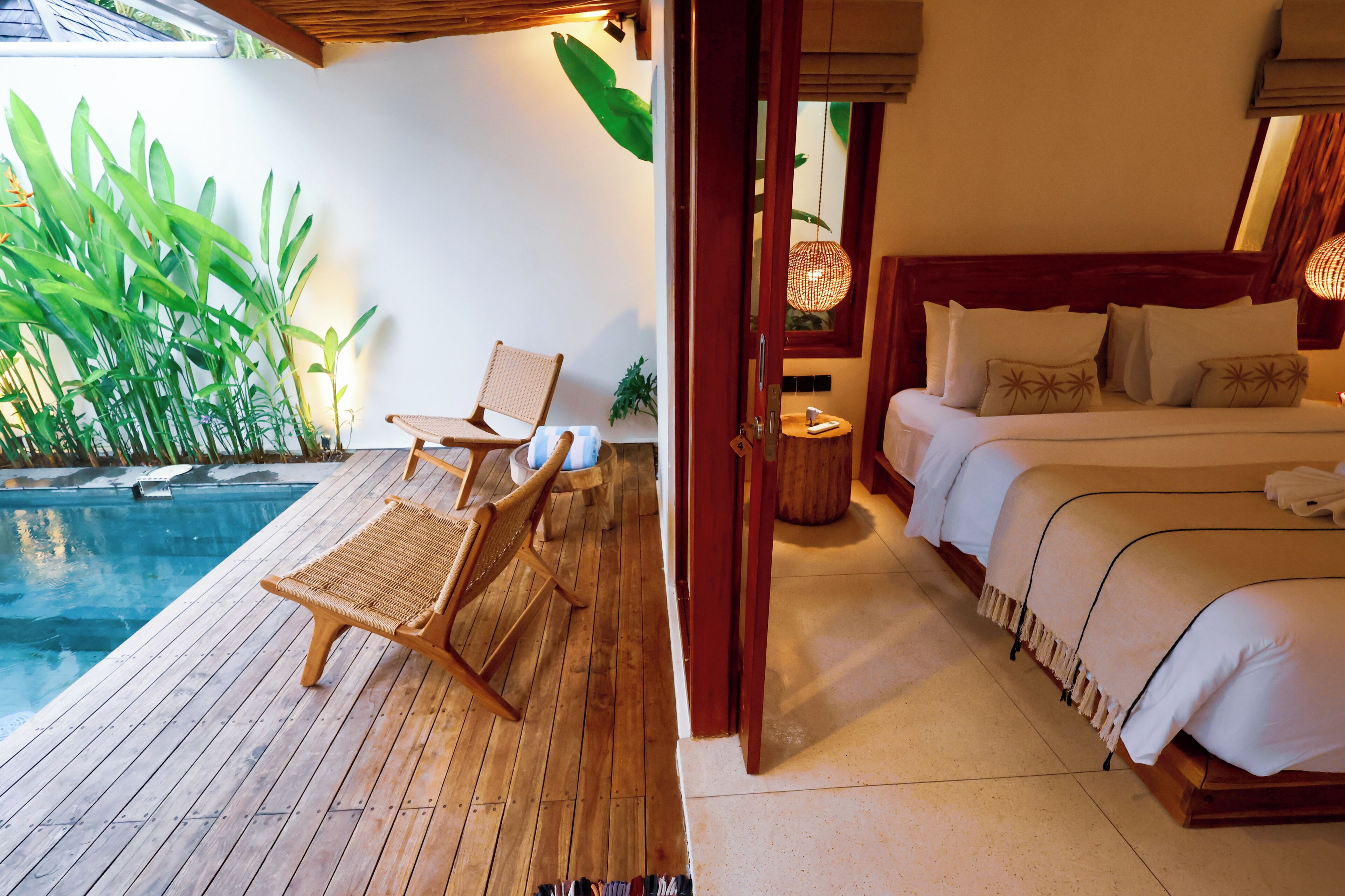 A wooden deck with a pool, a bed with white linens, and a wicker chair.