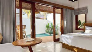 Camera d'albergo con un letto, un tavolo rotondo in legno, un'ampia finestra vista piscina e verde, e una porta scorrevole in vetro che dà su uno spazio all'aperto.