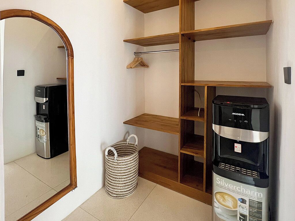 A compact room with a wooden shelving unit, a coffee machine, and a water dispenser.