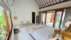 A bedroom with a large bed, a bedside table, a lamp, and a view of a pool and garden.