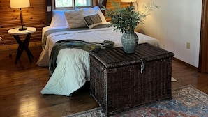 A cozy bedroom with a bed, bedside lamps, a wicker side table, a rug, and a hanging light fixture. - New! Quiet cabin in the pines at Custer State Park (Custer)