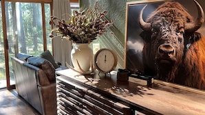 A room with a large window, a sofa, a clock, a potted plant, and a framed picture of a bull. - New! Quiet cabin in the pines at Custer State Park (Custer)