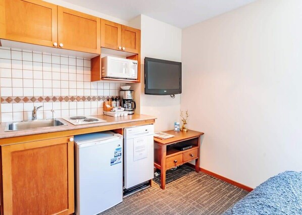 A compact kitchen with wooden cabinets, a microwave, a dishwasher, and a flat-screen TV mounted on the wall. - Entire Studio in Whistler Village Resort - Unit 437 (Whistler)