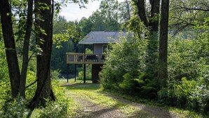 Una cabaña con terraza, rodeada de un bosque denso y un camino de grava.