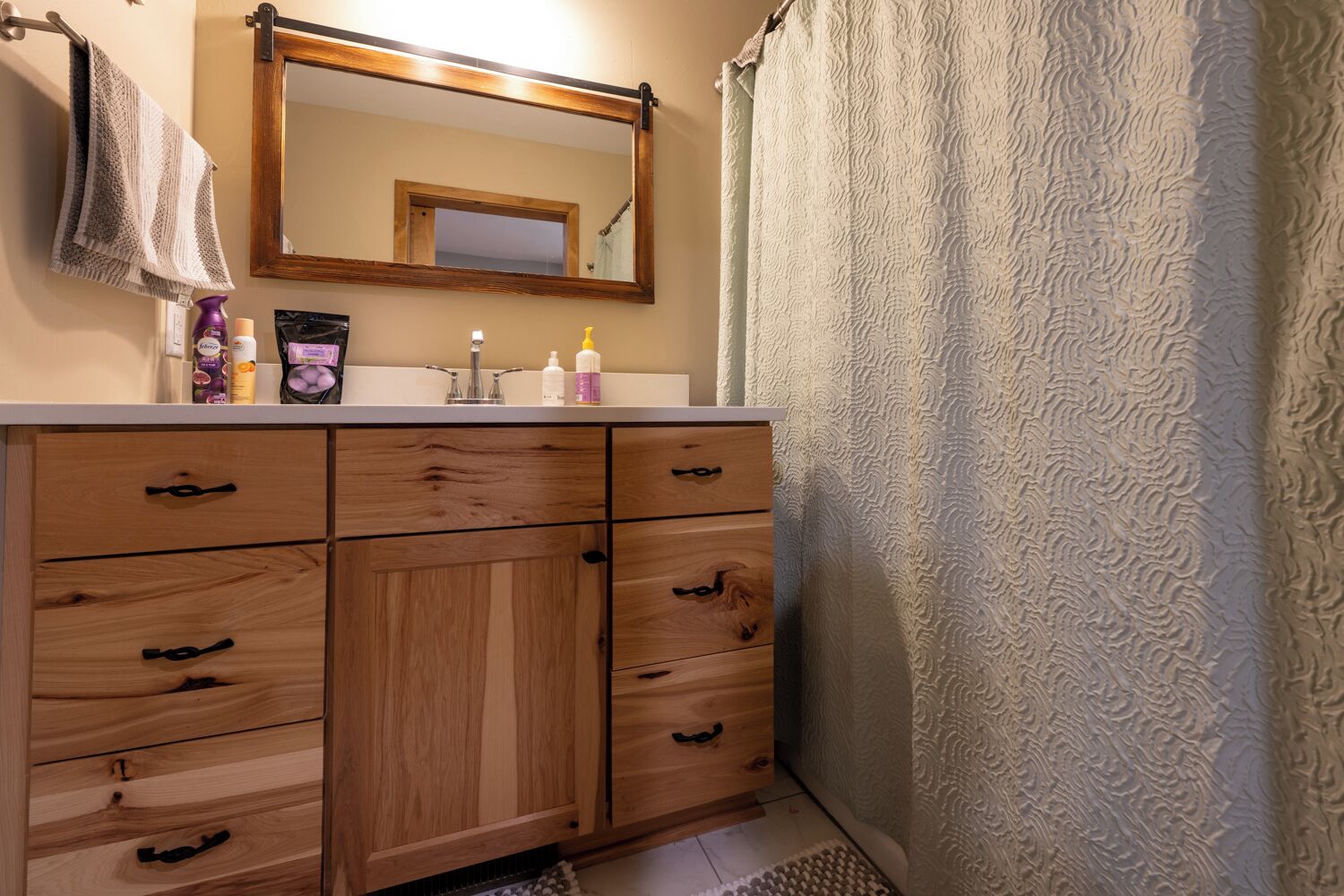 A bathroom with wooden cabinets, a mirror, and toiletries on the counter.