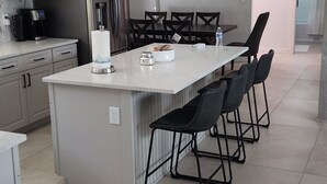 Una cocina moderna con una isla central, taburetes de bar, un refrigerador y una cafetera.