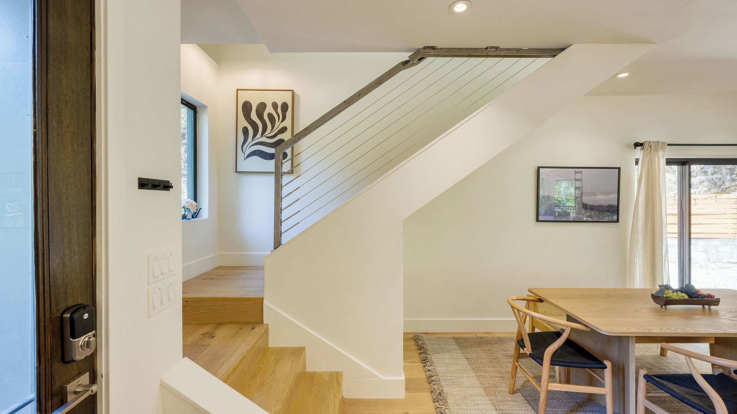 Un interior moderno con una escalera de madera, una zona de comedor con mesa y sillas, y obras de arte en las paredes.