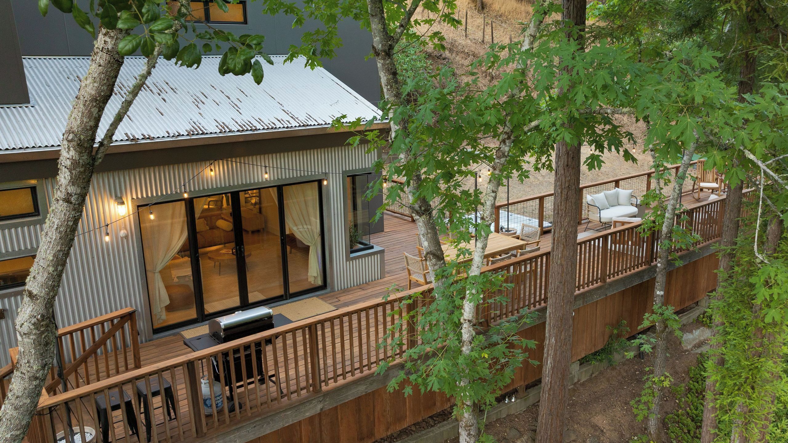 A modern house with a deck, large windows, and a view of the surrounding forest.