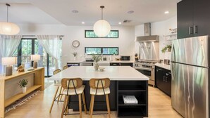 A modern kitchen with a central island, stainless steel appliances, and a dining area with wooden chairs. - Mill Creek by Avantstay Modern Design, Patio, Hot Tub (Healdsburg)