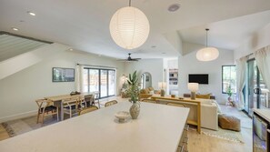 Un vaste espace de vie comprenant une grande table à manger, un ensemble de canapés et un téléviseur fixé au mur.