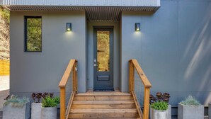 A modern building entrance with a wooden staircase, concrete planters with plants, and a grey door. - Mill Creek by Avantstay Modern Design, Patio, Hot Tub (Healdsburg)
