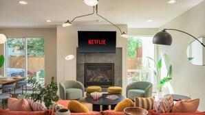 Una sala de estar moderna con chimenea, asientos cómodos y una gran pantalla de televisión que muestra "NETFLIX".