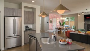 Una cocina moderna con electrodomésticos de acero inoxidable, una isla central con un lavamanos y un comedor con un televisor mostrando 'NETFLIX'.