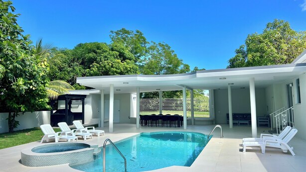 A modern outdoor swimming pool with lounge chairs and a covered patio area.