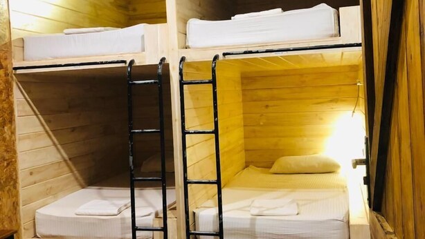 A wooden bunk bed room with two beds, a ladder, and a wooden wardrobe with drawers.
