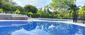 A swimming pool with a clear blue water surface, surrounded by a black metal fence and lush greenery. - Encantadora Casa Piscina Privada AA Wifi (Ricaurte)