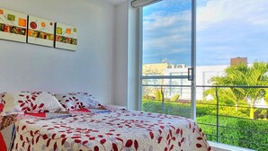 Un dormitorio con un ventanal grande, una cama con colcha estampada y una obra de arte colgada en la pared.