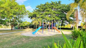 Un parque infantil con toboganes y estructuras para escalar, rodeado de árboles y césped.