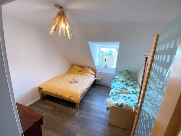 Ein kleiner, gemütlicher Raum mit einem Einzelbett, einem Fenster mit Blick auf Grünflächen und einer außergewöhnlichen Deckenleuchte.