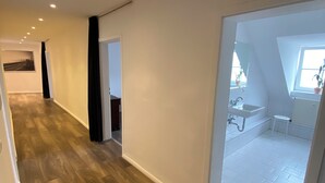 Ein geräumiger Korridor mit Holzboden, der zu einem Badezimmer mit Fenster und Waschbecken führt.