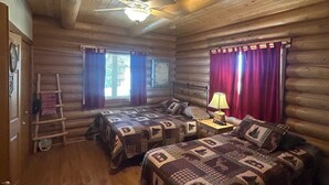Ein Schlafzimmer in einer Blockhütte mit zwei Betten, einem Deckenventilator und einer Leitern.