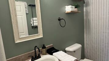 Ein Badezimmer mit weißem Waschbecken, Toilette, Spiegel und Duschvorhang.